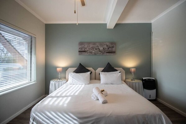 A hotel room with a bed, two bedside tables, a wall-mounted artwork, and a window with blinds.