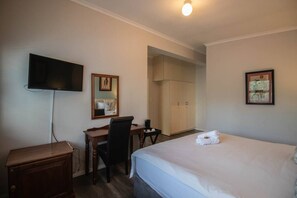 A hotel room with a bed, a desk, a chair, a television, and a wardrobe.