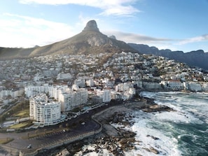 A coastal cityscape with a prominent mountain, residential buildings, and a rocky shoreline.