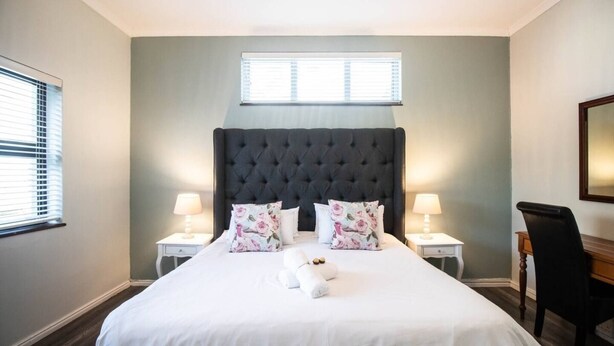 Une chambre d’hôtel avec un grand lit, deux tables de chevet avec des lampes, un bureau et une fenêtre avec des stores.