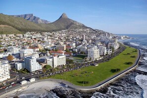 A coastal cityscape with a prominent mountain in the background, a beachfront promenade, and dense urban development.