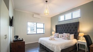 Une chambre à coucher avec un grand lit, une table de chevet, une commode et un téléviseur fixé au mur.