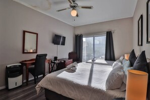 A hotel room with a bed, desk, chair, TV, and a large window with curtains. - Spring Tide Inn - Std family room 7 with balcony (Cape Town)