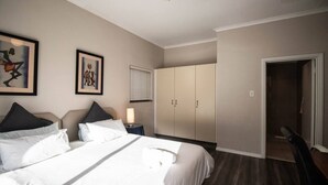 A hotel room with a bed, a nightstand, a lamp, a wardrobe, and a door leading to another room. - Spring Tide Inn - Std family room 7 with balcony (Cape Town)