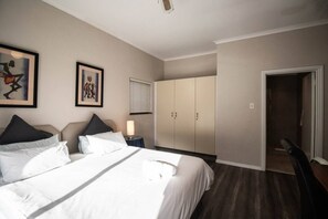 Una camera d'albergo con un letto, un comodino, una lampada, un armadio e una porta che dà su un'altra stanza.