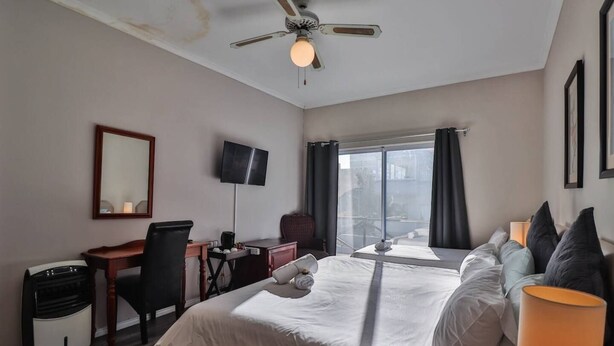 A hotel room with a bed, desk, chair, TV, and a large window with curtains. - Spring Tide Inn - Std family room 7 with balcony (Cape Town)