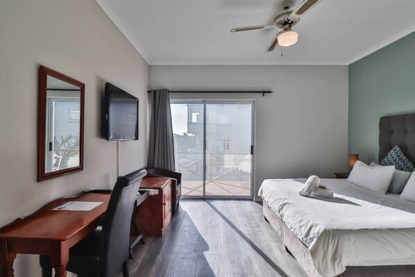 Une chambre d’hôtel avec un lit, un bureau, une chaise, une télévision et un balcon avec vue.