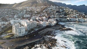 A coastal cityscape with a prominent mountain in the background, a beachfront with rocky terrain, and densely packed residential buildings. - Spring Tide Inn - Std King Room 8 with Balcony (Cape Town)
