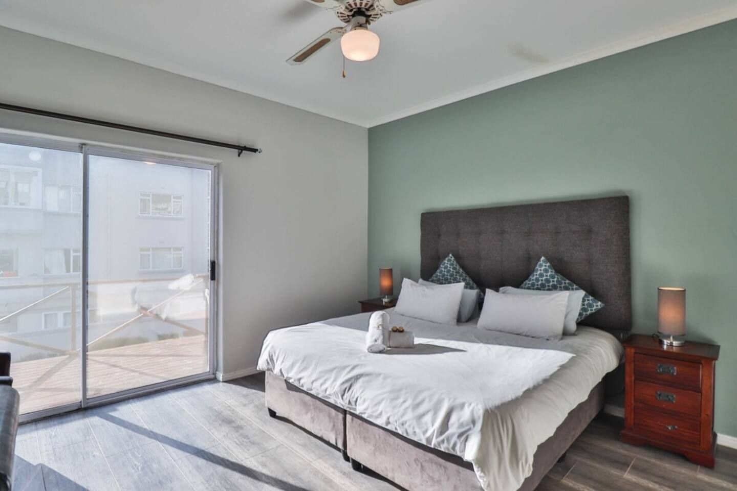 A bedroom with a bed, a nightstand, a ceiling fan, and a sliding glass door leading to an outdoor area.