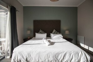 Une chambre d’hôtel avec un grand lit, deux tables de chevet, une tête de lit et une vue sur l’extérieur.