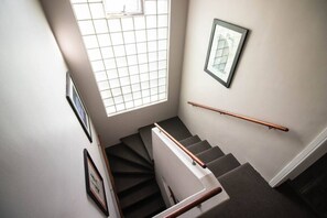 Un escalier avec une rampe, une fenêtre à carreaux et des tableaux encadrés accrochés aux murs.
