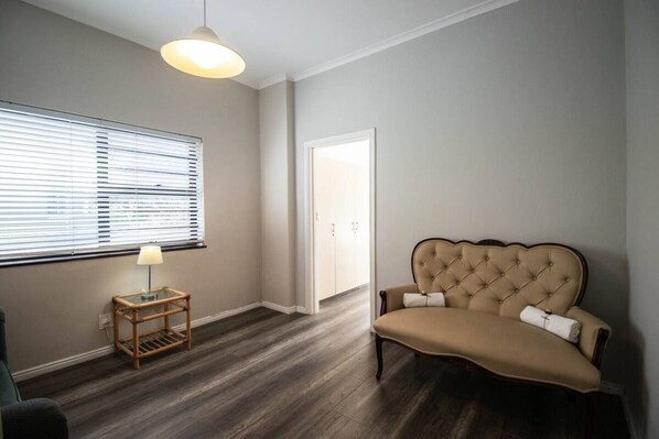 Une pièce comprenant un canapé, une lampe, une fenêtre avec des stores et une porte.