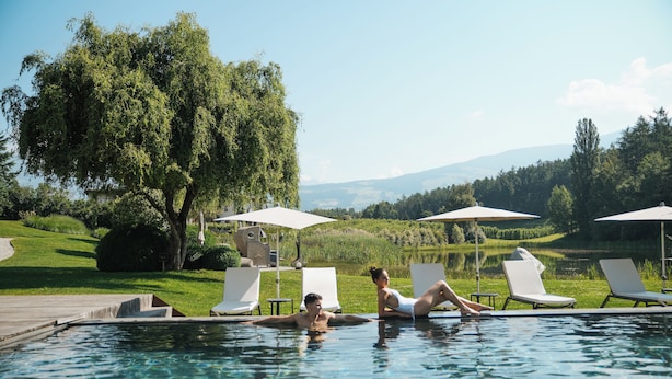A pool area with lounge chairs and umbrellas, surrounded by greenery and a view of hills. - Seehof Nature Retreat (Naz Sciaves)