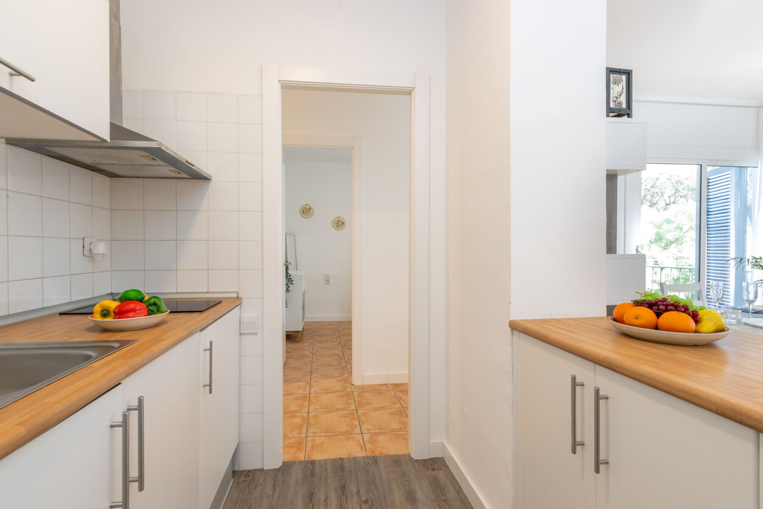Moderni keittiö, jossa on valkoiset kaapit, puinen työtaso ja näkymä ruokailutilaan.