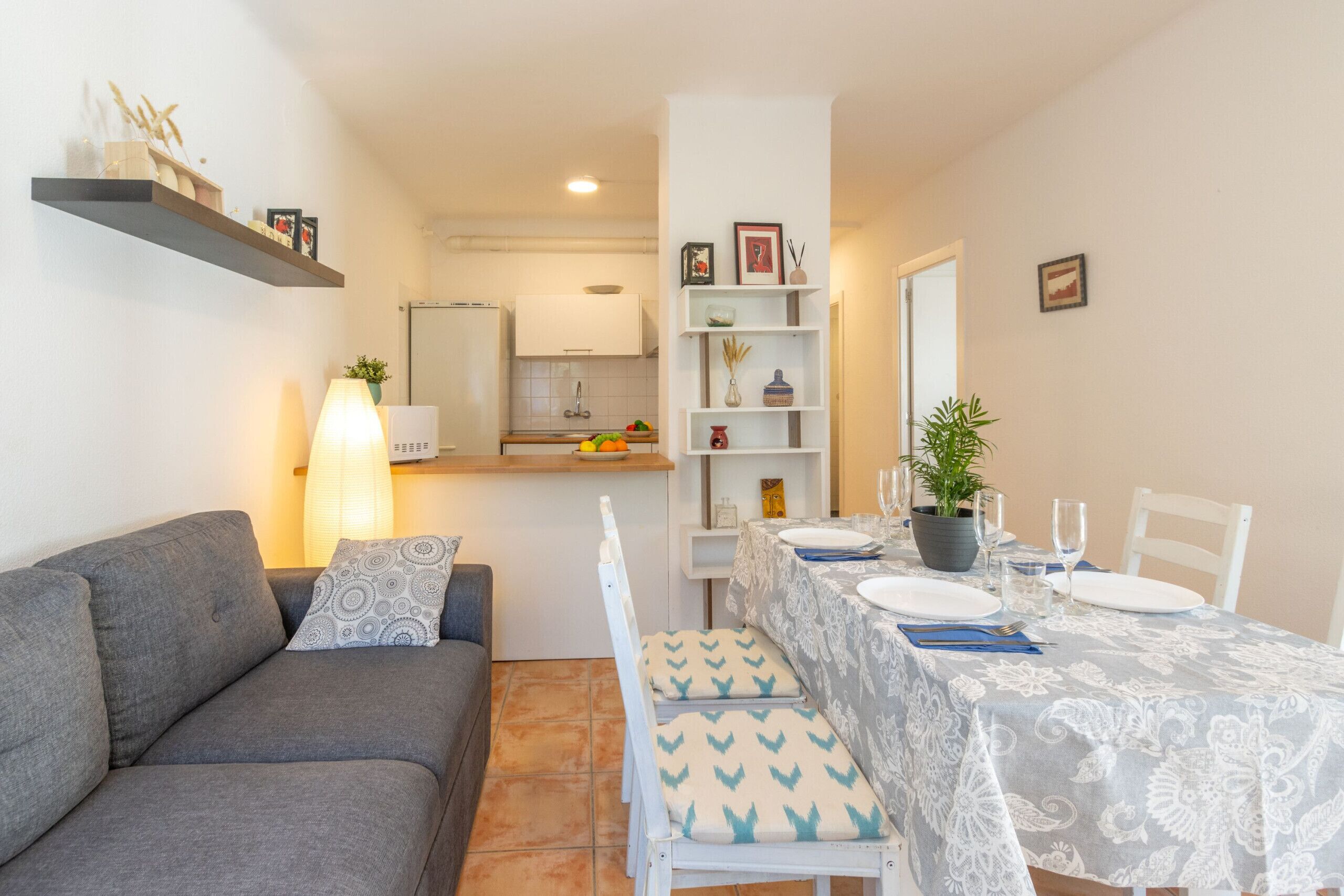 Ein modernes Wohnzimmer mit einem grauen Sofa, einem Esstisch für zwei Personen und einer Küche im Hintergrund.