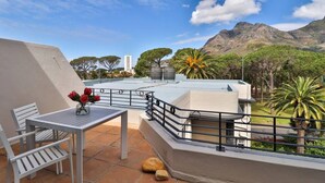 Una terraza en la azotea con mesa y sillas, barandilla y vistas a montañas y árboles.