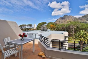 Una terrazza sul tetto con tavolo e sedie, una ringhiera e vista sulle montagne e sugli alberi.