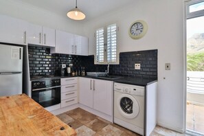A compact kitchen with white cabinets, a black countertop, a built-in oven, a dishwasher, and a window with blinds.