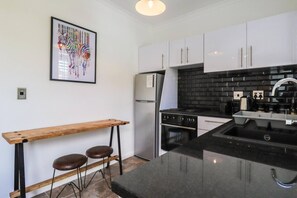 A compact kitchen with a black countertop, white cabinets, a stainless steel refrigerator, and a wooden bench with stools.