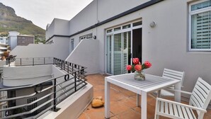 Una terraza con una mesa y sillas blancas, un pequeño jarrón con flores y una escalera que lleva a un nivel superior.