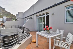 Una terrazza con tavolo e sedie bianche, un piccolo vaso con fiori e una scala che conduce a un livello superiore.