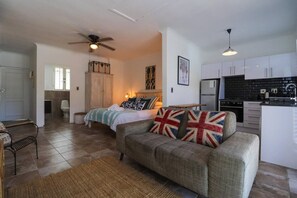 A compact living space with a sofa, a bed, a kitchen area, and a ceiling fan.
