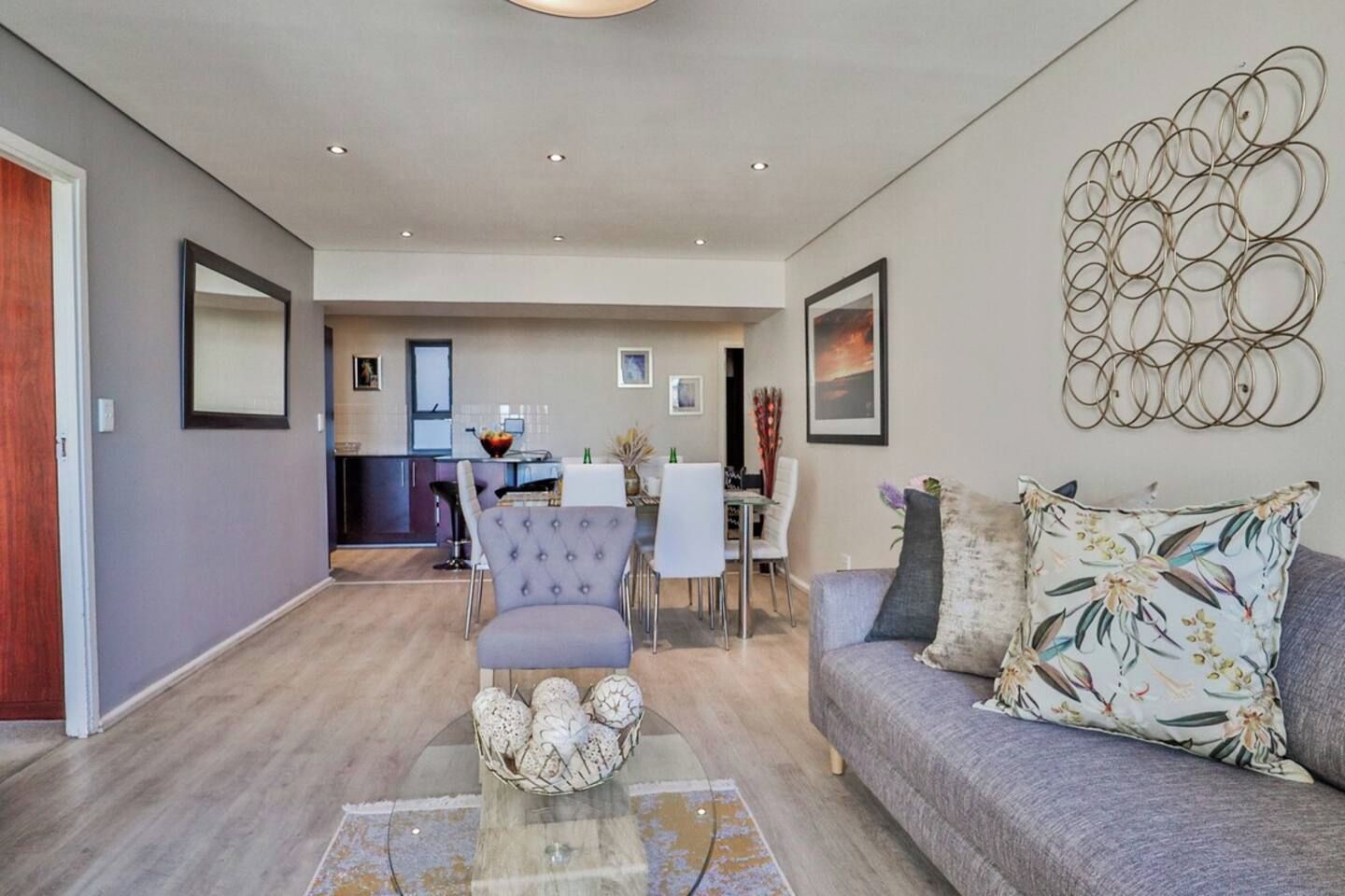 A modern living room with a grey sofa, a coffee table with decorative items, and a dining area with a white table and chairs.