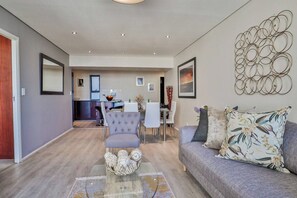 A modern living room with a grey sofa, a coffee table with decorative items, and a dining area with a white table and chairs.