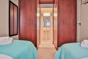A hotel room with two beds, a bathroom with a sink, and wooden wardrobes.