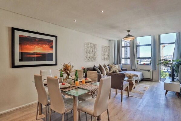 A modern living room with a dining area, large windows, and a city view.