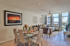 A modern living room with a dining area, large windows, and a city view.