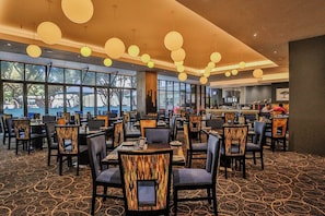 A spacious dining area with multiple tables and chairs, large windows, and hanging spherical light fixtures.