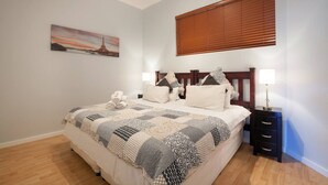 A bedroom with a bed, bedside tables, a nightstand, a window with blinds, and a painting on the wall. - Piazza on Church 906 by Ctha (Cape Town)