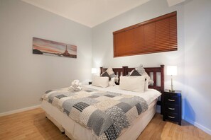 Una camera da letto con un letto, comodini, un tavolo da notte, una finestra con tende e un quadro appeso al muro.