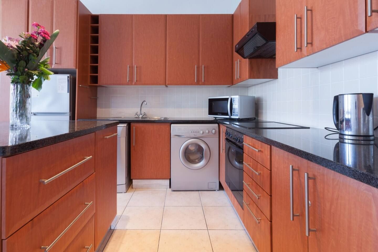 A modern kitchen with wooden cabinets, a washing machine, a microwave, and a kettle.