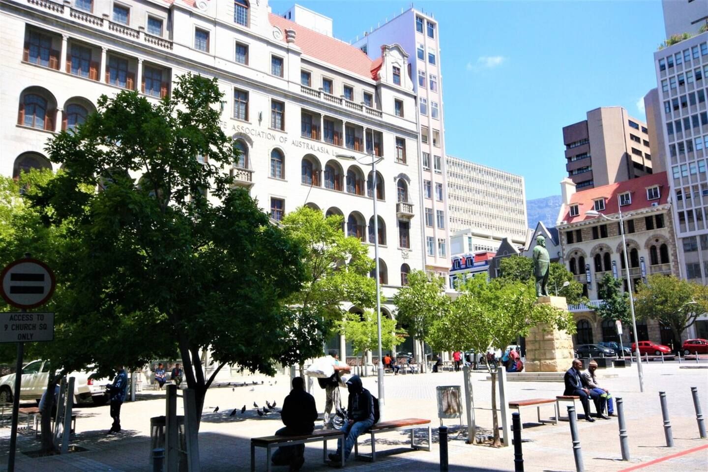 A public square with benches, a statue, and a building with arched windows.