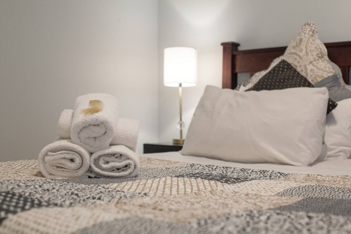 Un lit bien fait, avec des serviettes blanches pliées en rouleau, un plaid à motifs et une lampe de chevet.