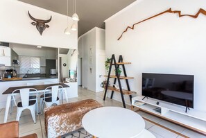 A modern living room with a dining area, a TV, and a kitchen in the background.