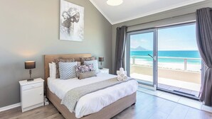 Une chambre à coucher avec un lit, des tables de chevet, un tableau et une vue sur la plage.