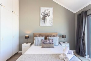 A bedroom with a bed, two bedside tables, a headboard, a wall-mounted artwork, and a window with curtains.