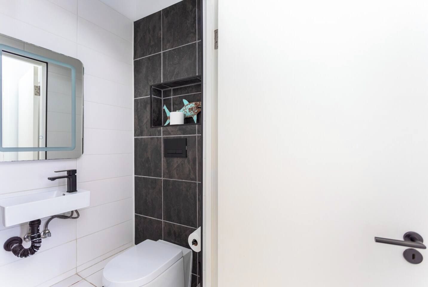 A bathroom with a white sink, black faucet, and a toilet. There is a mirror with a lighted frame above the sink.