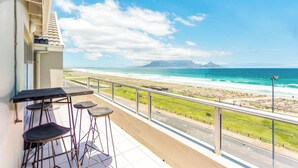 Un balcon avec vue sur la plage et l’océan, une table et deux tabourets de bar.
