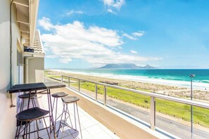 Un balcone con vista sulla spiaggia e sull'oceano, un tavolo e due sgabelli da bar.