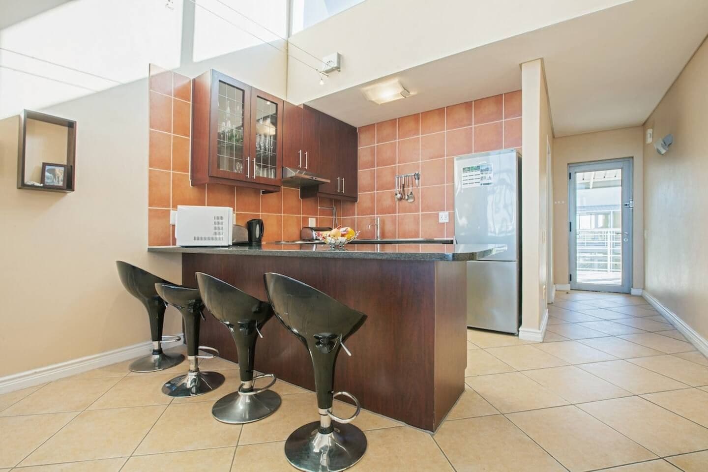 A modern kitchen with a central island, bar stools, and a refrigerator.