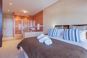 A hotel room with a large bed, a shower area, and a bathroom with a sink and mirror. - 3br Coastal Stay | Balcony, bbq & views by Ctha (Cape Town)