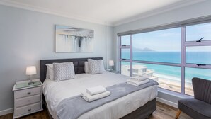 Una camera da letto moderna con un letto grande, un comodino, una sedia e vista sull'oceano.