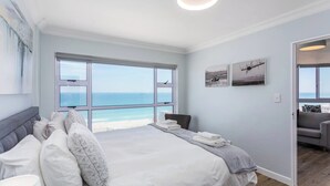 A bedroom with a large bed, a view of the beach, and a door leading to another room. - Ocean View A1101 by Ctha (Cape Town)