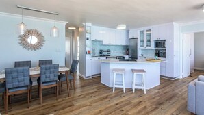 A modern kitchen with white cabinets, a central island, and bar stools. - Ocean View A1101 by Ctha (Cape Town)