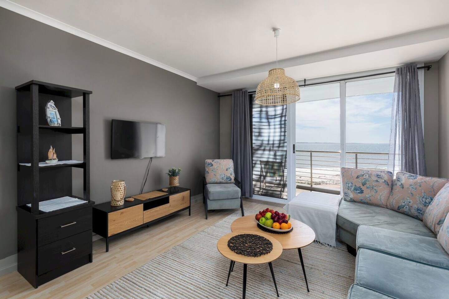 A modern living room with a sofa, a coffee table with fruit, a TV, and a bookshelf.