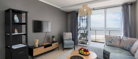 A modern living room with a sofa, a coffee table with fruit, a TV, and a bookshelf.
